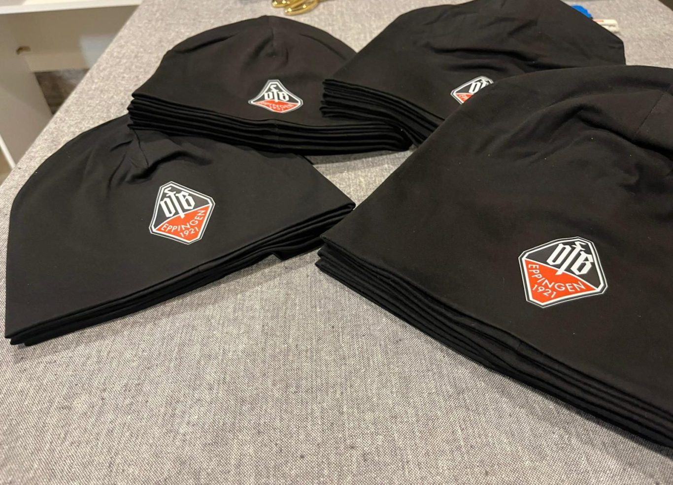 Logo Druck Schwarze Mützen mit einem farbigen Logo, auf einem flachen Untergrund angeordnet.